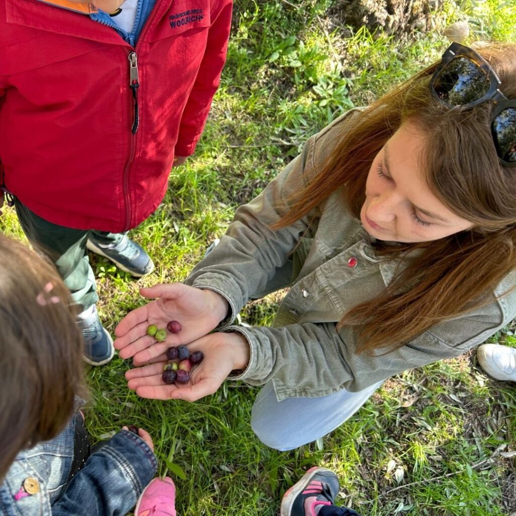 Maria Viola Bonafini tiene per le mani alcune olive mostrandole a dei bambini interessati.