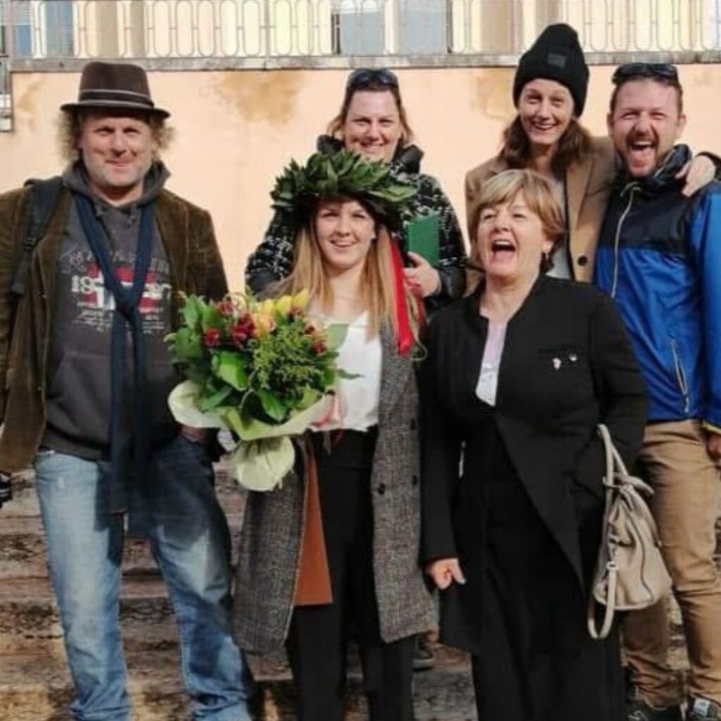 Maria Viola Bonafini con corona di alloro in testa e mazzo di fiori in mano festeggia il conseguimento della laurea con i propri familiari.