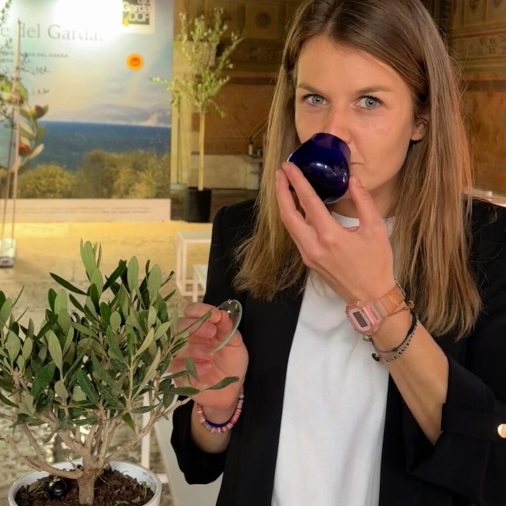 Maria Viola Bonafini in primo piano sta portando all'olfatto un bicchiere di olio con una piccola piantina di ulivo vicino a lei