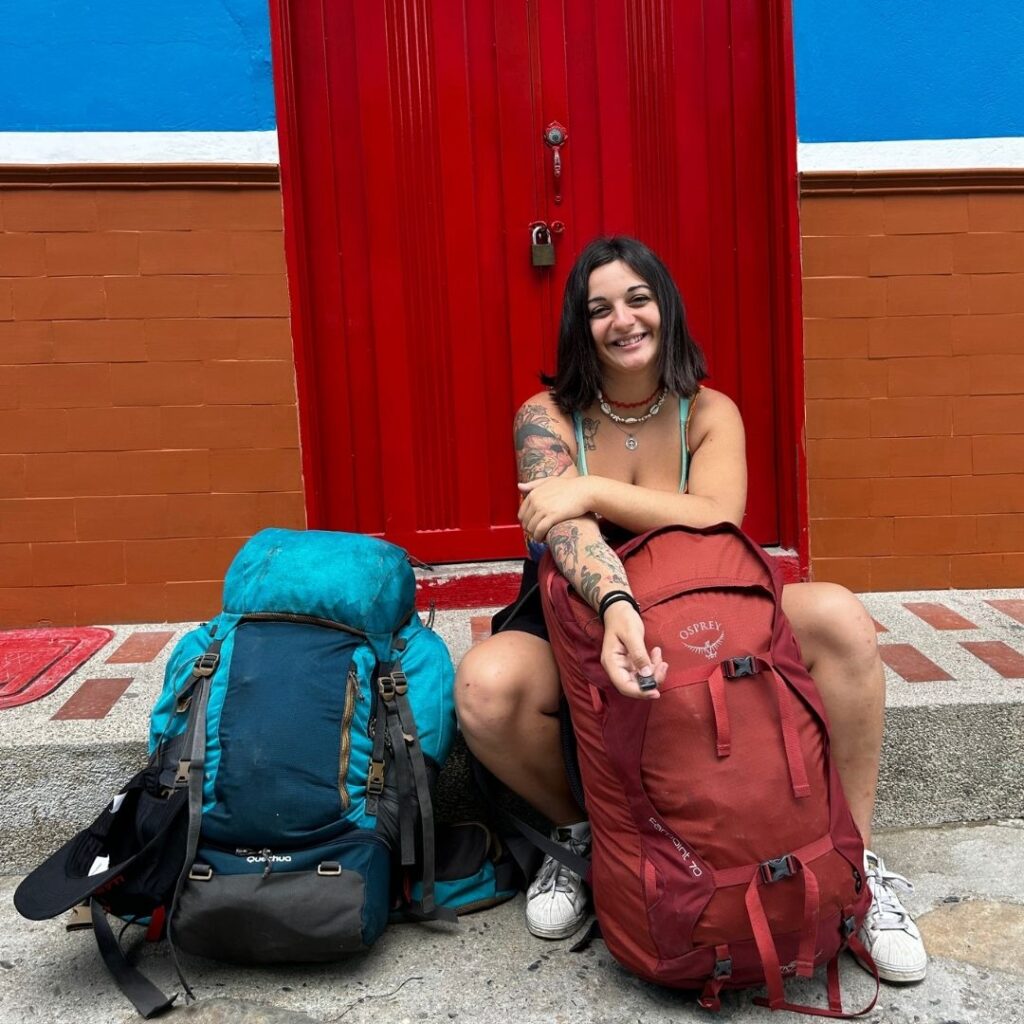 Irene De Pascalis seduta su un marciapiede con i suoi borsoni da viaggio